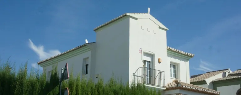 Helles Einfamilienhaus hinter einer Hecke unter blauem Himmel