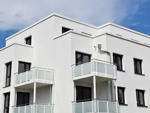 Helle Wohnanlage mit Glasbalkonen vor blauem Himmel